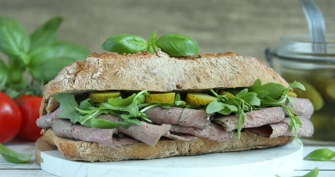 Woman putting delicious sandwich with pastrami (cured beef meat) and taking pickle at table, closeup