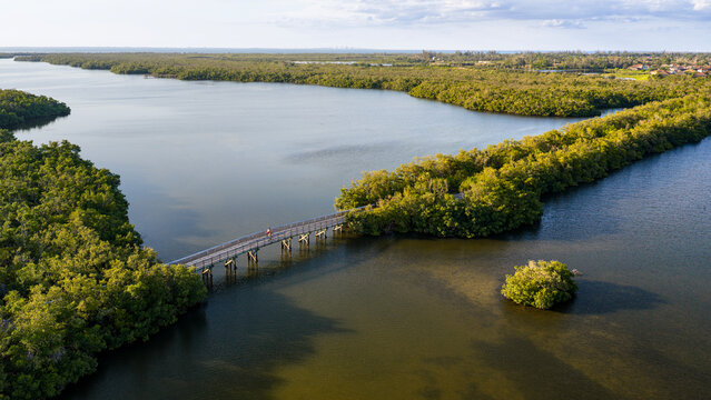 Golden hour aerial view of a scenic wooden footbridge crossing Perico Bayou at Robinson Preserve in Bradenton, FL. Tranquil waters and vibrant wetlands create a stunning coastal sunset.