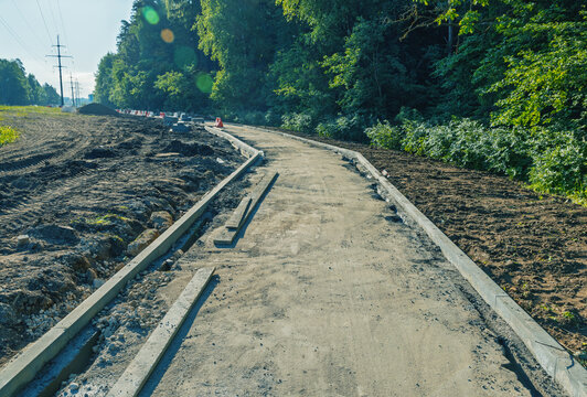 Rural road under construction with concrete curbs and forest edge