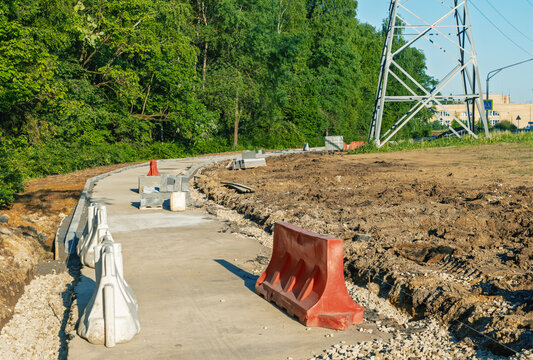 Temporary roadside barrier and unfinished concrete path beside construction clearing