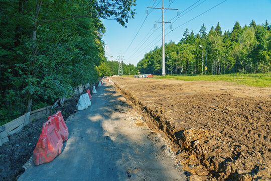 Rural roadside trench and utility poles beside forest clearing under blue sky