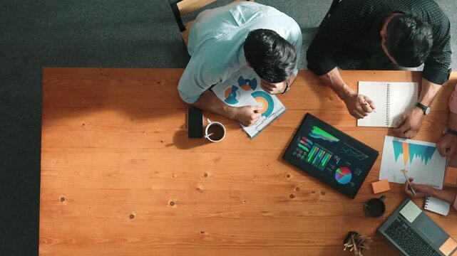 Executive manager explain financial graph to colleague at meeting room. Top aerial view of diverse marketing team sharing idea and planning strategy while sitting at table with tablet. Convocation.
