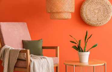 Armchair and houseplant on table near orange wall in room, closeup