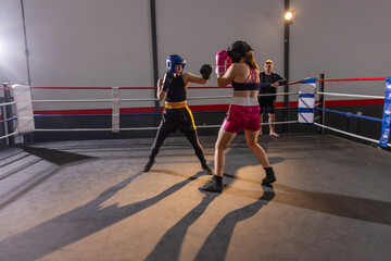 Fototapeta premium Male and female boxers sparring in ring with gloves; trainer watching from ropes under lights