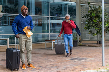 Two African American men, senior and twenty-something standing and walking on plaza with suitcases © wavebreak3
