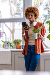 African American adult woman standing by kitchen counter holding mint-green mug checking smartphone © wavebreak3