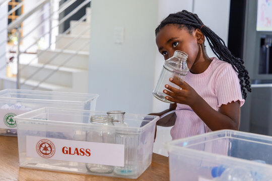 African American child holding glass jar sorting into bin labeled GLASS on kitchen counter