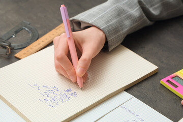 Naklejka premium Woman writing math formulas in notebook at dark table, closeup