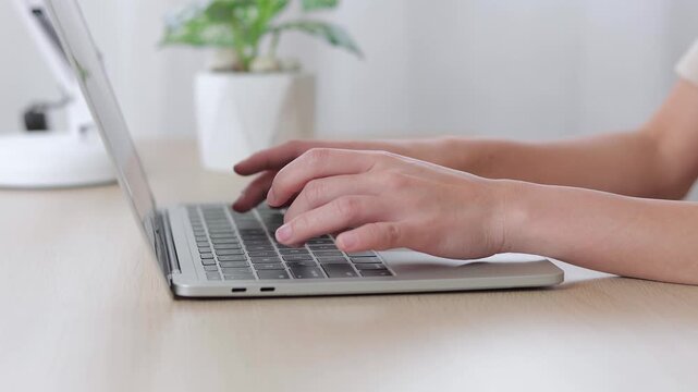 Close-up of a person typing on a laptop keyboard at a wooden desk, working from home or office. Concept of remote job, online learning, technology, and professional digital workspace.