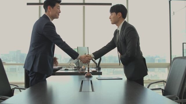 Two professional businessmen in suits shaking hands across a conference table with a scale of justice, symbolizing a successful legal agreement, partnership, or fair deal in a modern office setting.