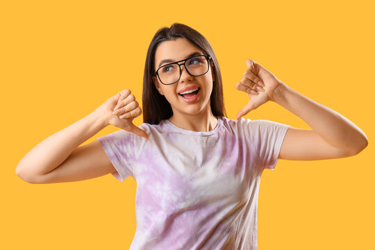 Pretty young woman wearing glasses and showing thumb-down on yellow background