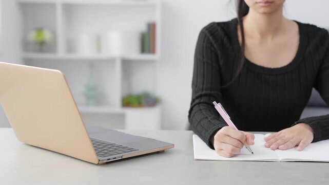 部屋でノートパソコンを見ながら勉強する女性