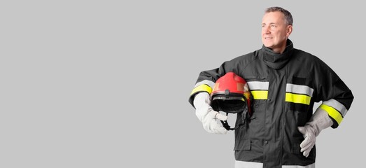 Fototapeta premium Smiling firefighter in protective gear holding red helmet, safety and emergency services professional, isolated on gray background