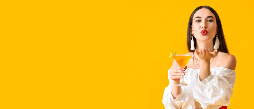 Beautiful young woman with cocktail blowing kiss on color background