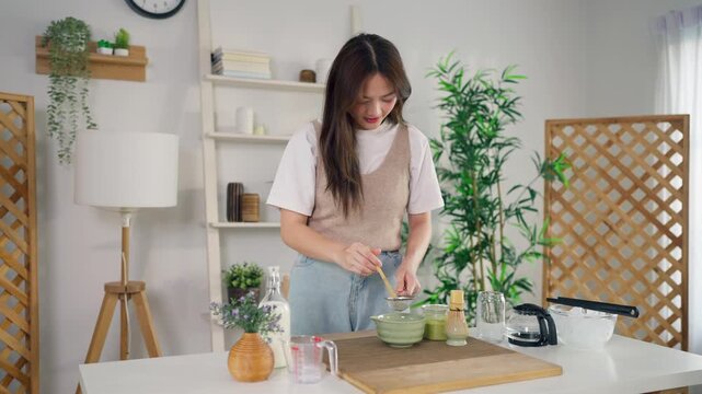 Asian young woman preparing matcha by stirring green tea powder in bowl. 