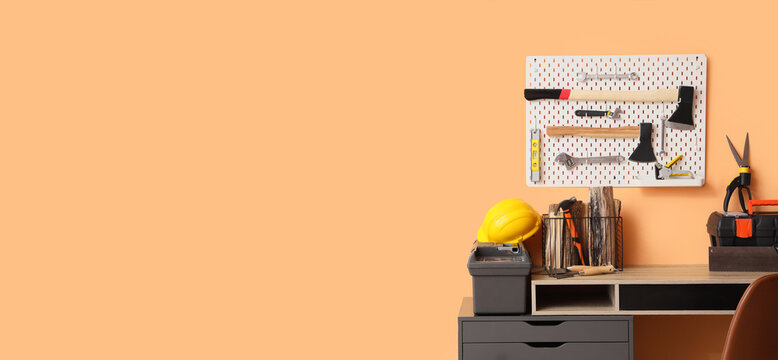 Home workshop desk with pegboard tool organization, construction safety helmet, and toolbox on peach wall background