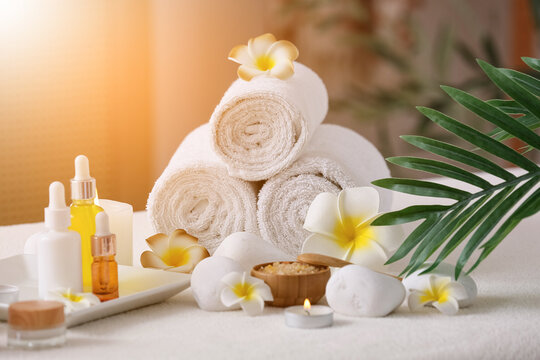 Plumeria flowers, clean towels and bottles of cosmetic products on white couch in interior of bathroom, closeup