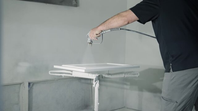 Professional wood worker paints kitchen cabinetry with a paint sprayer in workshop. Perfect for cabinetry, renovation, woodworking, and home improvement visuals.