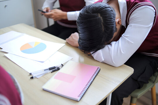Tired Male Student Sleeping on His Desk During Class or Exam with Pie Chart Paperwork Nearby