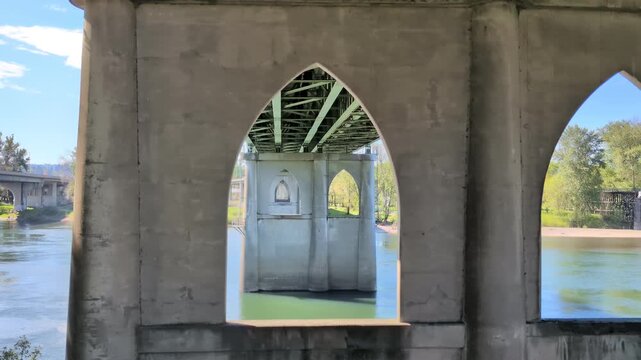 Video explores the underside of bridges, highlighting repeating concrete supports, flowing river views, and layered transportation infrastructure along the waterfront.
