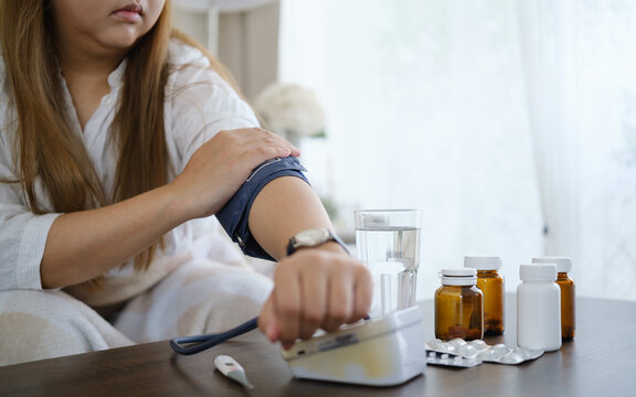 Woman measuring blood pressure at home beside prescription bottles and tablets, ideal for health checkup, disease prevention, and self-care concept.