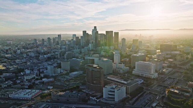 Cinematic aerial view of downtown Los Angeles skyline at golden hour with morning mist and freeway traffic.