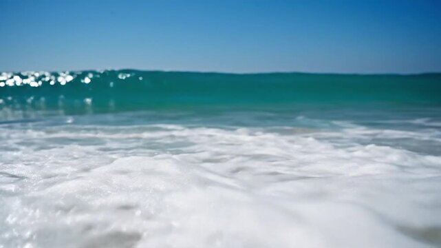 Waves lapping on the beach with turquoise sea in bright sunlight during midday near the shoreline