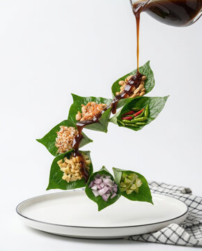 Miang Kham traditional Thai snack ingredients served on green leaves with pouring brown sauce