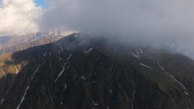 Aerial view of rugged Himalayan mountain ridge with scattered snow streaks below low clouds near Sar Pass Trek and Parvati Valley, Himachal Pradesh, India.