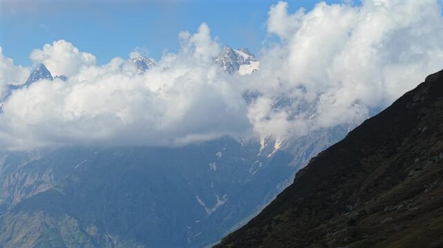 Cinematic aerial view of snow covered Himalayan mountains beneath thick white clouds, Sar Pass Trek, Parvati Valley, India
