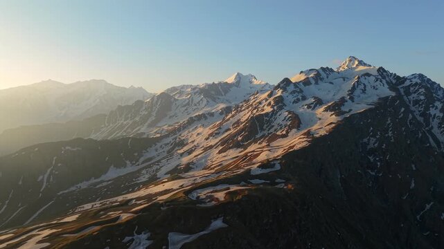 Dolly in aerial view over Himalayan mountains rugged alpine terrain with melting snow patches toward dramatic snow-covered peaks near Sar Pass Trek, Kasol, Himachal Pradesh, India.