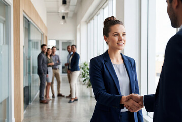 Fototapeta premium Confident young businesswoman in a blue suit shaking hands with a colleague in an office