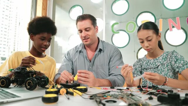 Skilled teacher teaching diverse students fixing car model by using wire and electronic equipment. Girl studying about using electrical tool to check mother board while looking at laptop. Edification