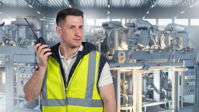 Industrial maintenance. Plant technician uses radio for communication while monitoring machinery inside production facility.