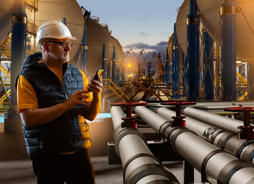 Chemical plant. Industrial engineer monitors pipeline systems and storage tanks using mobile technology at an energy terminal facility.