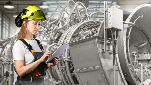 Industrial engineering. Female technician checks turbine equipment and complex machinery using a tablet at a manufacturing facility.