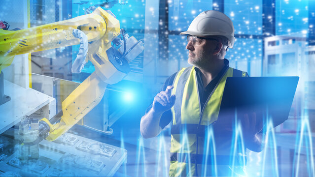 Industrial robotics. Engineer monitors robotic arm automation and production data using a laptop in a smart factory.