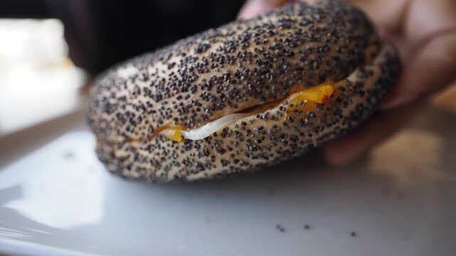 Enjoying a poppy seed bagel with filling at a cafe