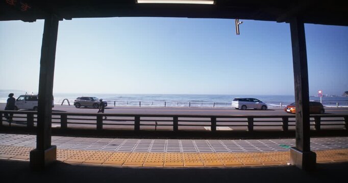 Silhouette Of Green and Yellow Tram Arriving at Coastal Platform With Ocean Behind - Wide Shot