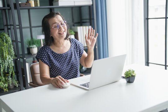 Senior Asian woman Work from home. smiling Beautiful mature&nbsp;asian woman VDO Call Conference talk chat online on video call on laptop webcam with technology concept.