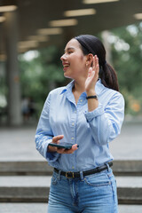 Fototapeta premium Young woman listening attentively with raised hand outdoors