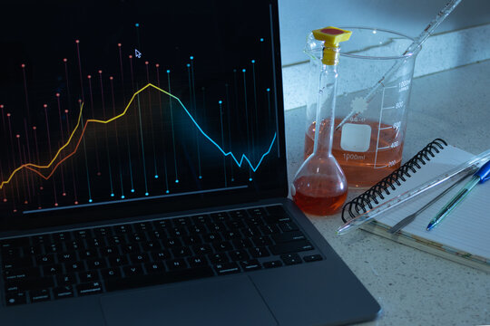 Scientist in a modern lab analyzes statistical charts on a laptop amid beakers, flasks and instruments, combining chemistry experiments with data driven research and e learning
