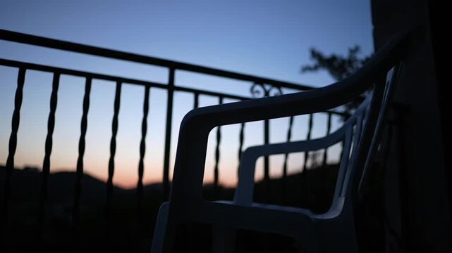 A solitary white plastic chair sitting on a balcony at twilight.