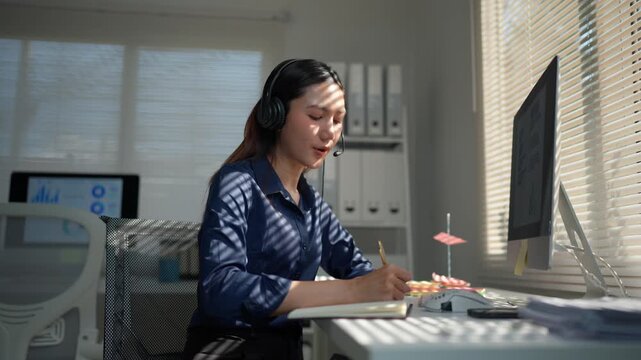 Professional female operator wearing a headset and talking to a client. Positive call center employee taking notes during a consultation