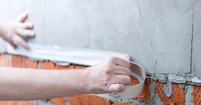 Hands apply waterproof sealant to brick wall joint