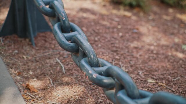 Close up view of heavy metal chain in park showing durable connected links with shallow depth of field in an outdoor setting