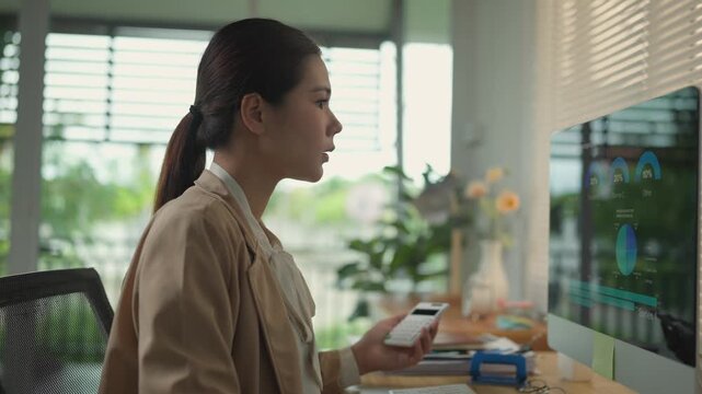 Side view of a young asian woman working as an accountant. Businesswoman using a calculator and computer to check financial data