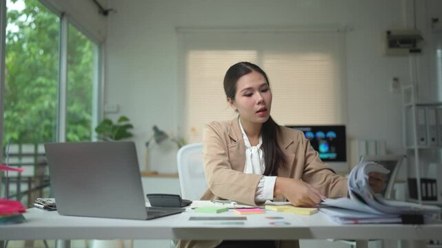 Young professional woman feeling frustrated and overwhelmed while searching for a specific paper in a large stack of documents on her desk