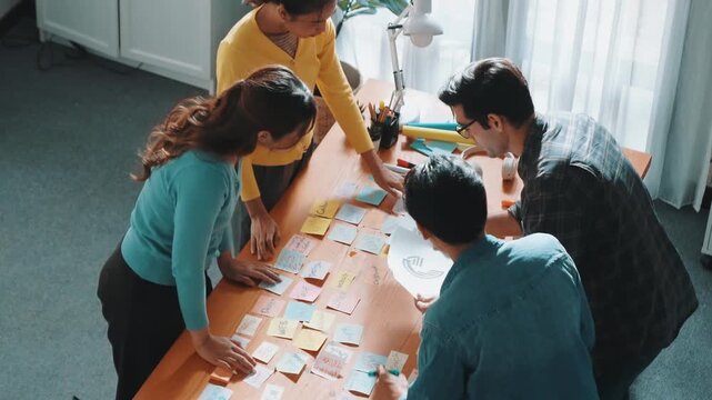 Top view of skilled designer explain and brainstorming idea for logo design and writing concept. Aerial view of business people discuss and talking while using sticky notes sharing idea. Symposium.