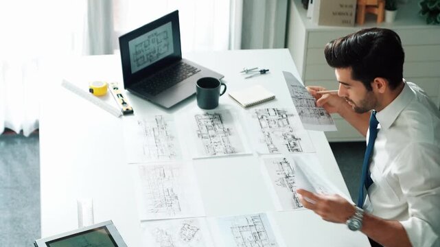 Architect engineer using laptop planning house design at office while sitting at meeting table with blueprint and equipment scatter around.Skilled civil engineer working at blueprint. Alimentation.